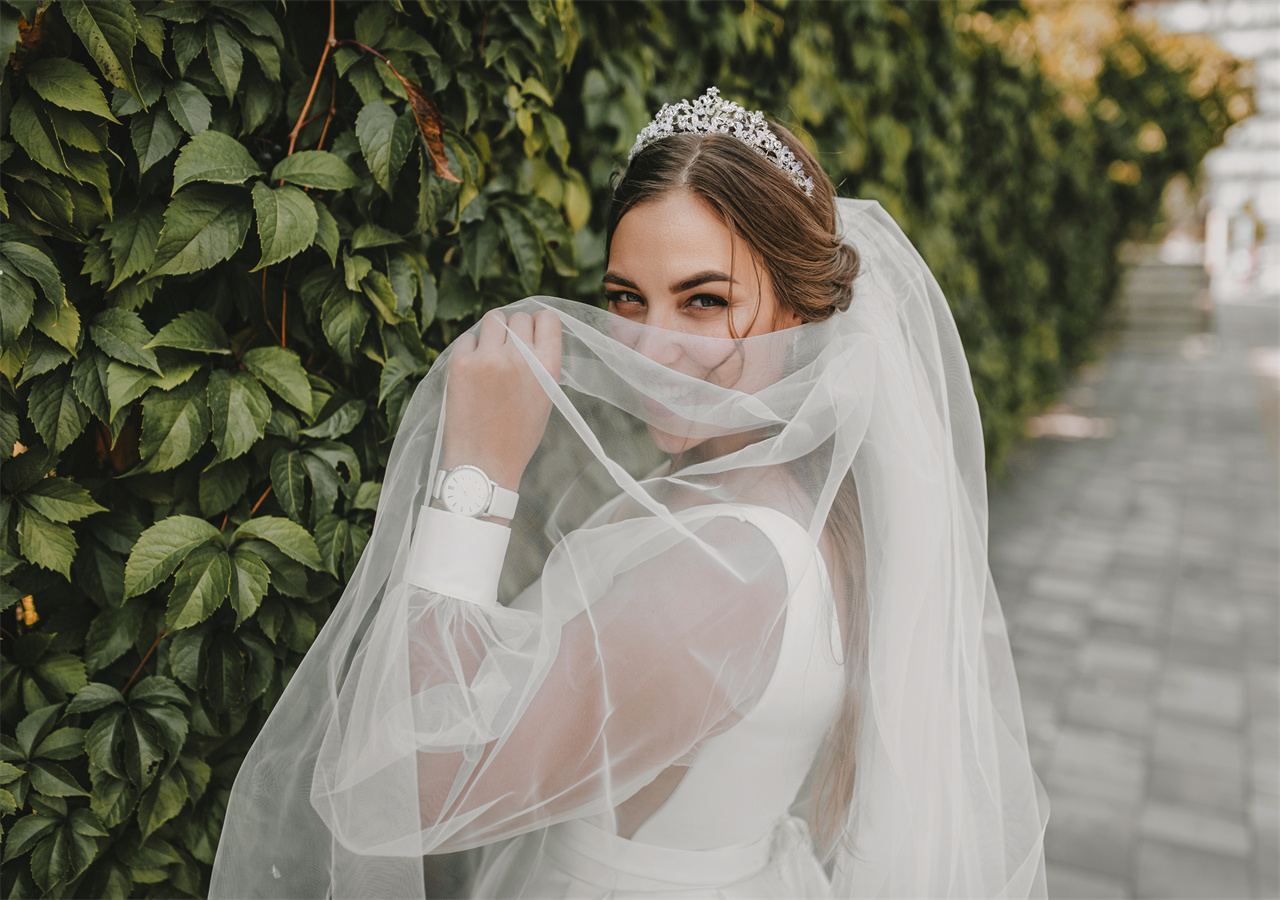 A bride in her Sweetv tiara Bridal wedding dress, covering her mouth with mesh and smiling.